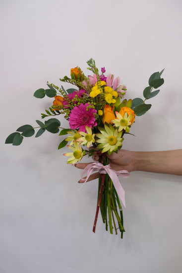 Bouquet of colorful flowers held by a hand against a plain background