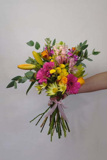 Bouquet of colorful flowers held by a person against a plain background