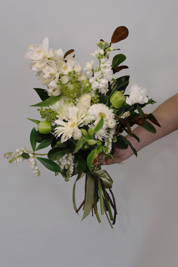 Bouquet of white and green flowers held by a person against a plain background