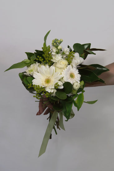 Bouquet of white and green flowers held by a hand against a plain background