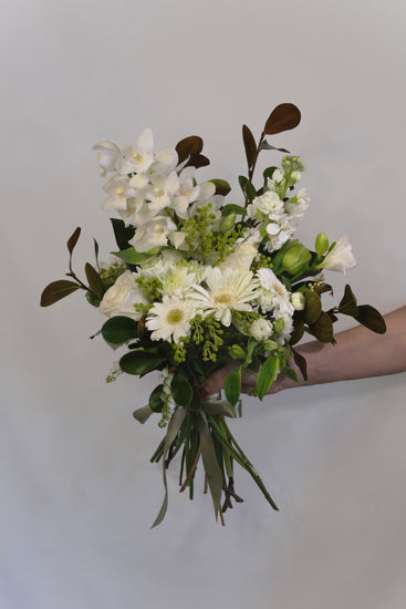 Bouquet of white and green flowers held against a plain background